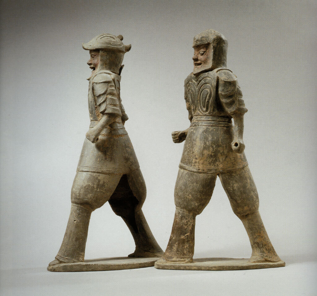 Two Striding, Armor-Clad, Bearded Warriors Wearing Helmets With Protective Neck And Ear Flaps, One With Mouth Open, One With Mouth Closed, Their Hands Positioned To Hold Weapons