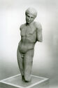 A marble sculpture depicts a youthful male body in a contrapposto pose with losses at the knees, shoulder, and elbow.