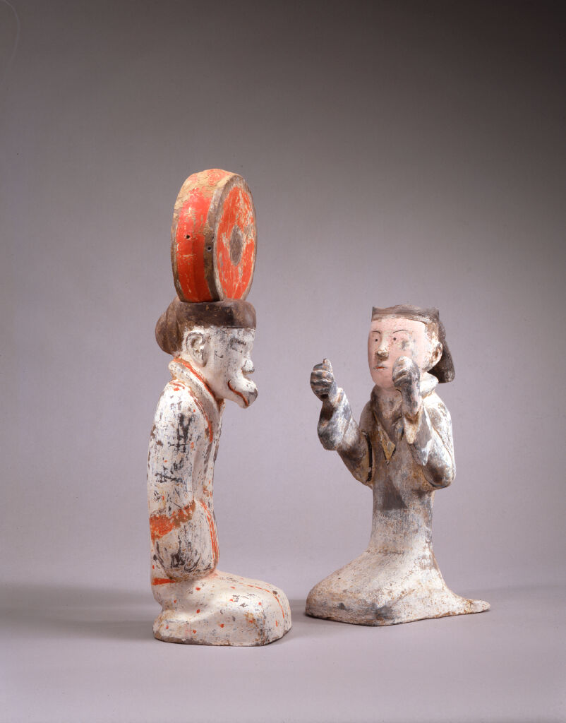 Kneeling Female Figure Beating A Circular Drum On A Stand In The Form Of A Kneeling Human With A Bird's Beak (Or Wearing A Bird Mask)